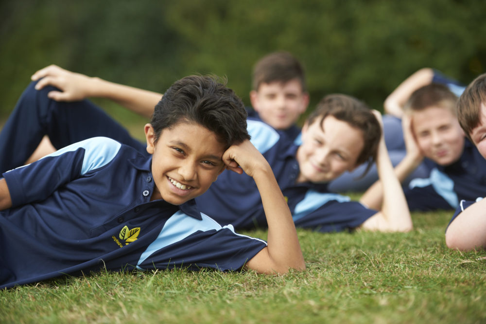 Small group of Leigh Academy Longfield students pose for the camera in their PE kits, whilst laying on the grass.